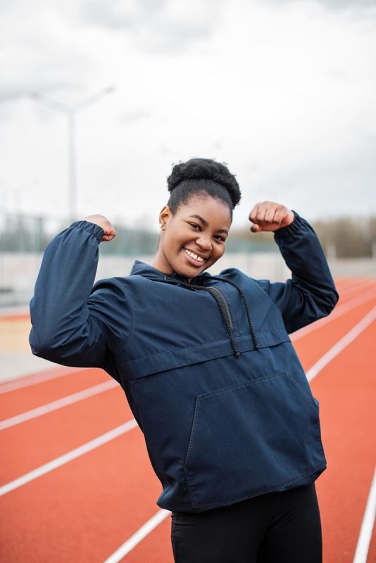A woman flexes her muscles on an outdoor track, promoting fitness and a healthy lifestyle.