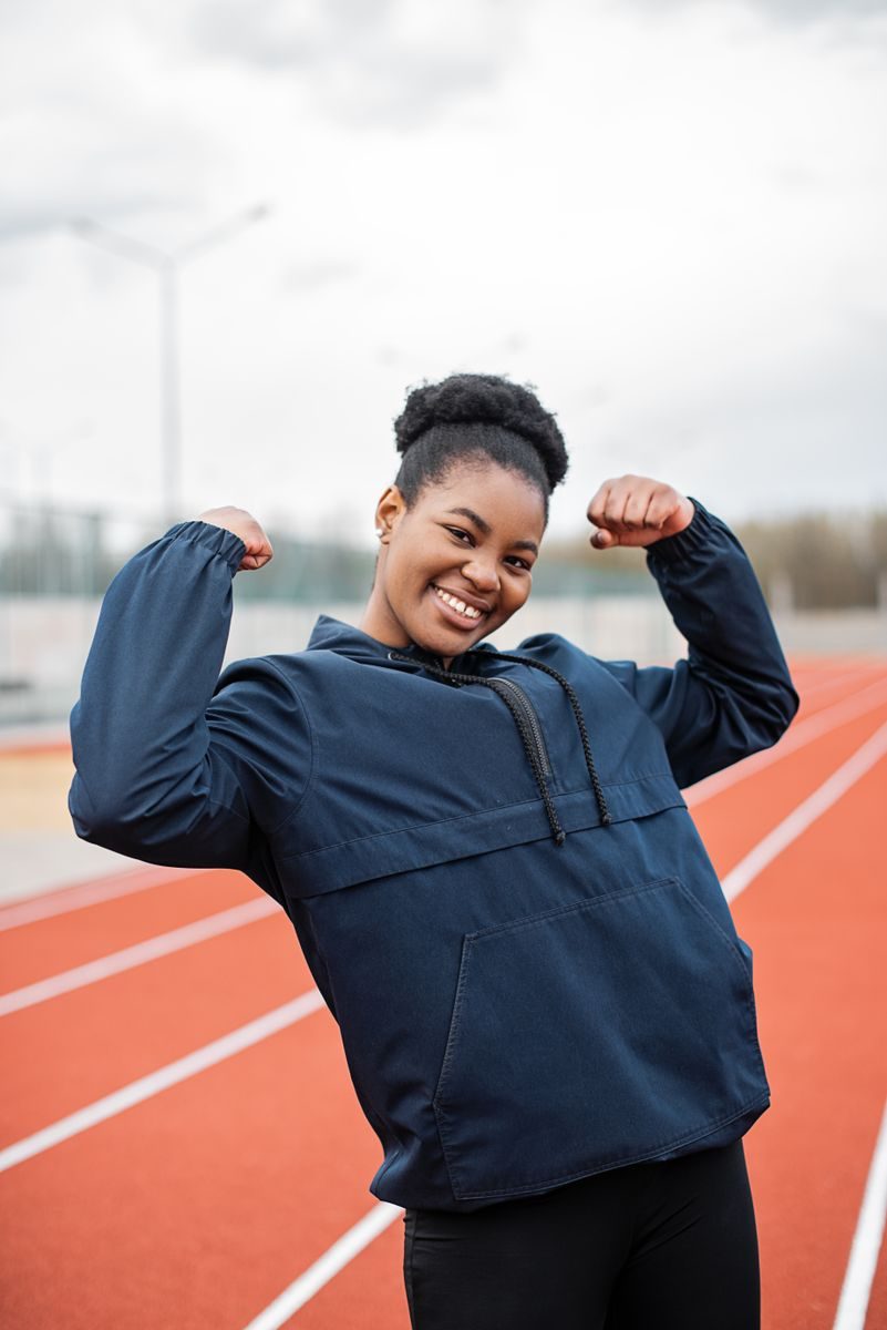 A woman flexes her muscles on an outdoor track, promoting fitness and a healthy lifestyle.