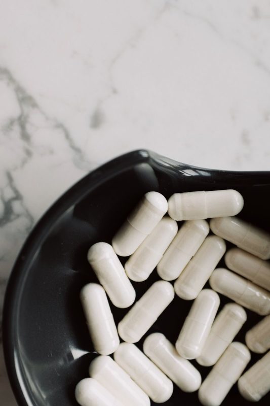 A close-up view of white capsules in a black bowl on a marble surface.