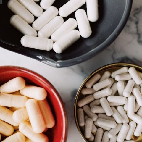 Top view of assorted white and beige capsules in colorful bowls placed on a marble surface.