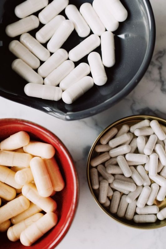 Top view of assorted white and beige capsules in colorful bowls placed on a marble surface.