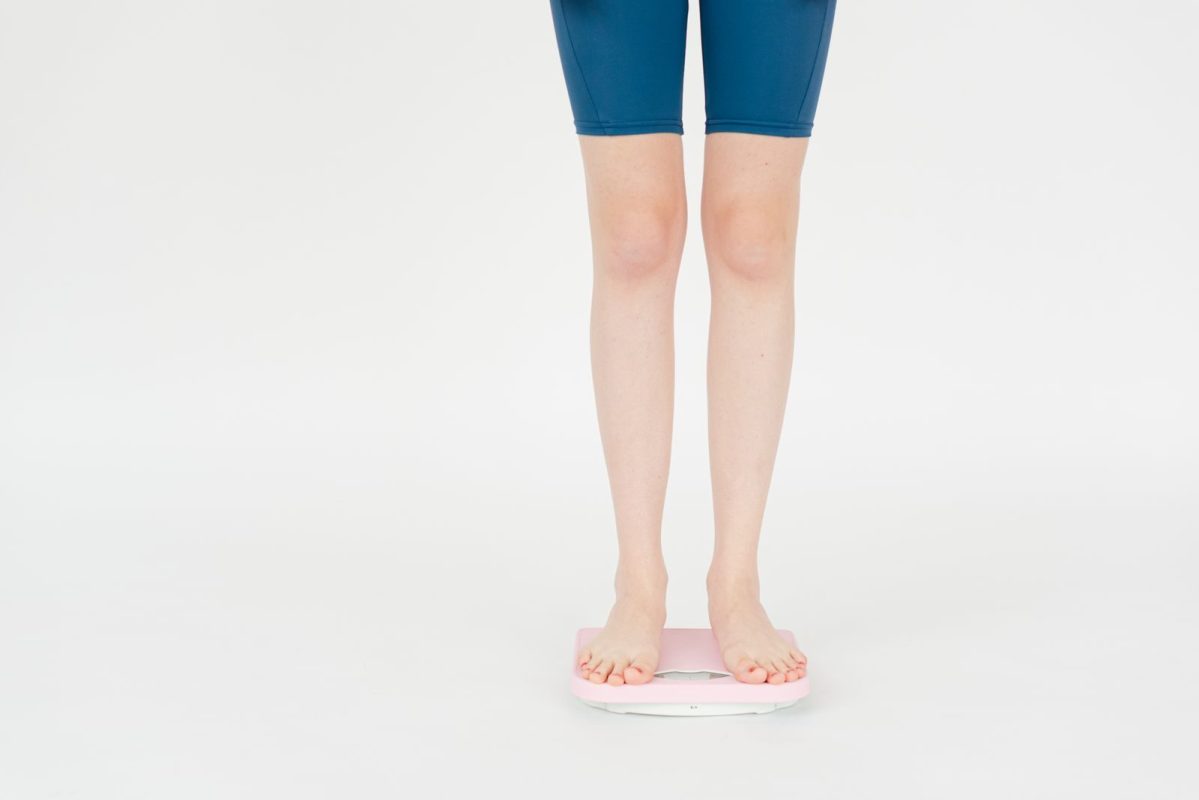 Woman in sportswear measuring weight on scales against white background