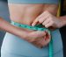 Close-up of a woman measuring her waist with a tape, representing fitness, health, and weight loss.